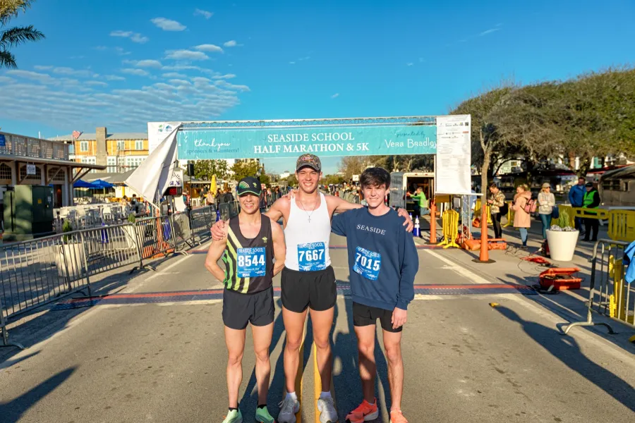 Three young men pose for a photo under the Seaside School Half Marathon & 5K finish line banner.