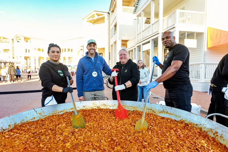 Four people standing around a large pot of food, holding large cooking utensils.