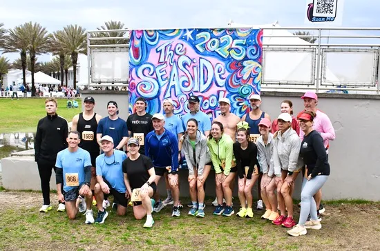 A group of runners posing for a photo in front of a colorful "The Seaside School" banner.