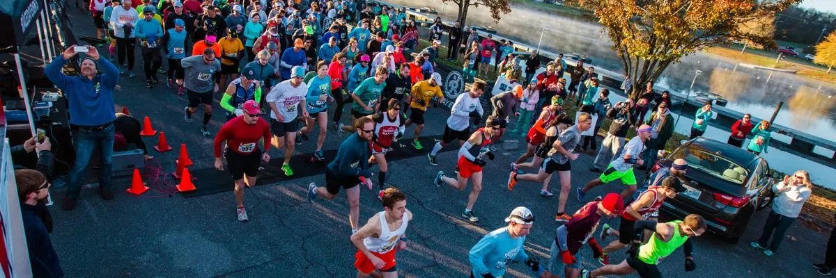 A large group of runners are starting a race, with many in motion and some spectators on the side.