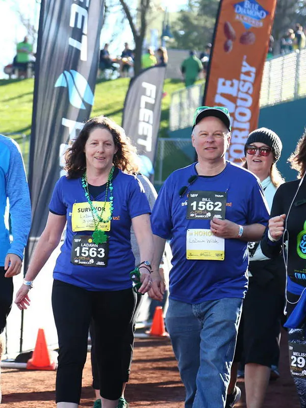 A group of runners, including a couple in the foreground wearing blue shirts and bibs, walking towards the camera at a race event.