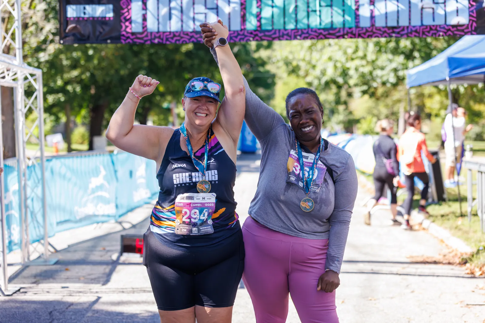 Two women celebrating at the finish line of a half marathon, holding hands and wearing medals.