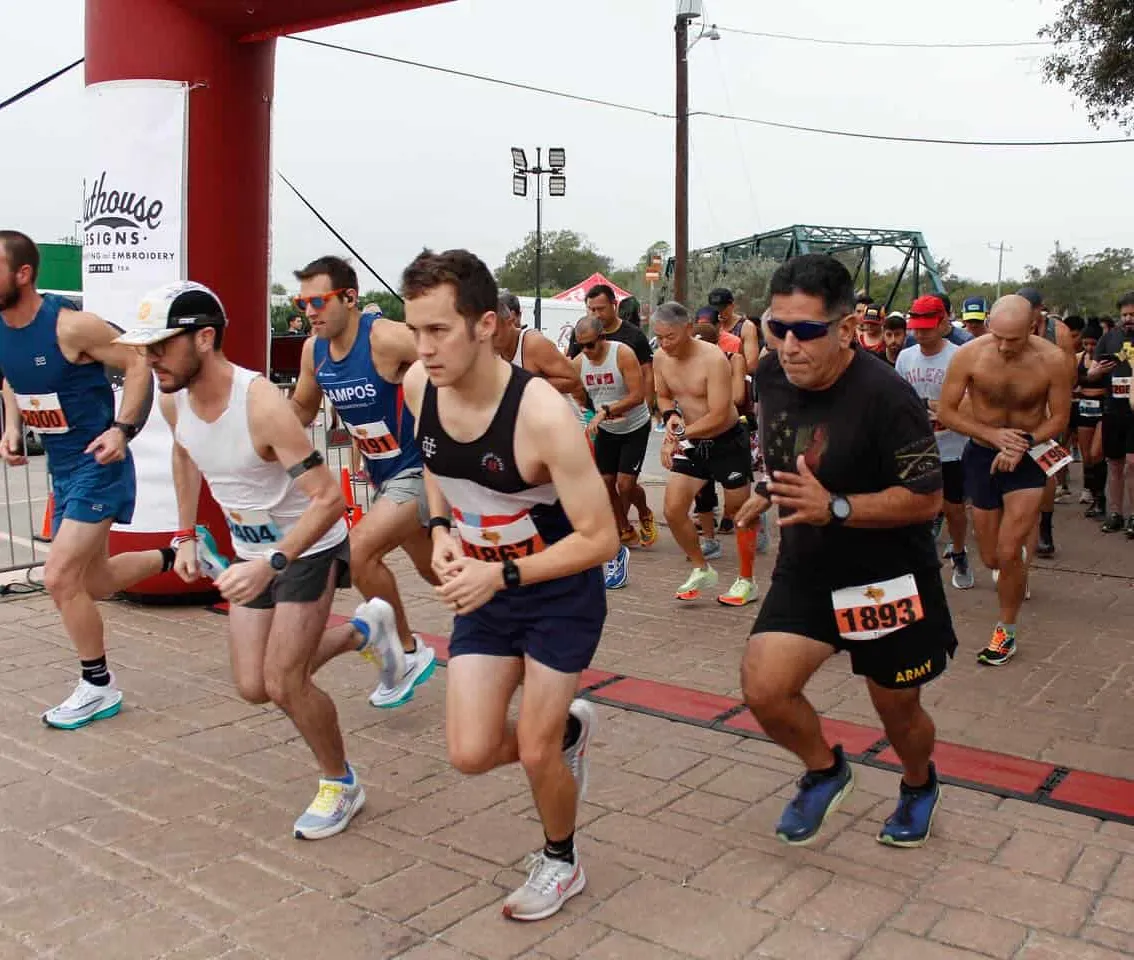 Runners starting a race, with a red archway at the start line and a bridge in the background.