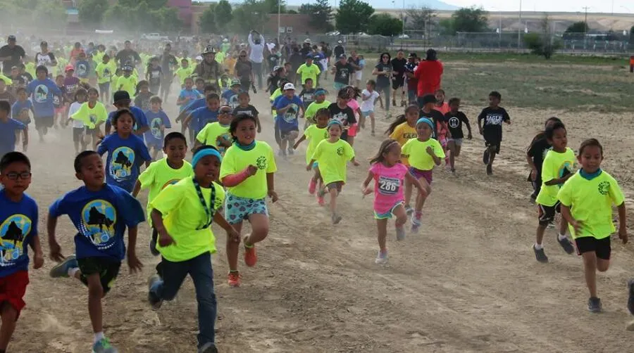 A large group of children running on a dirt path during a race, many wearing bright yellow shirts.