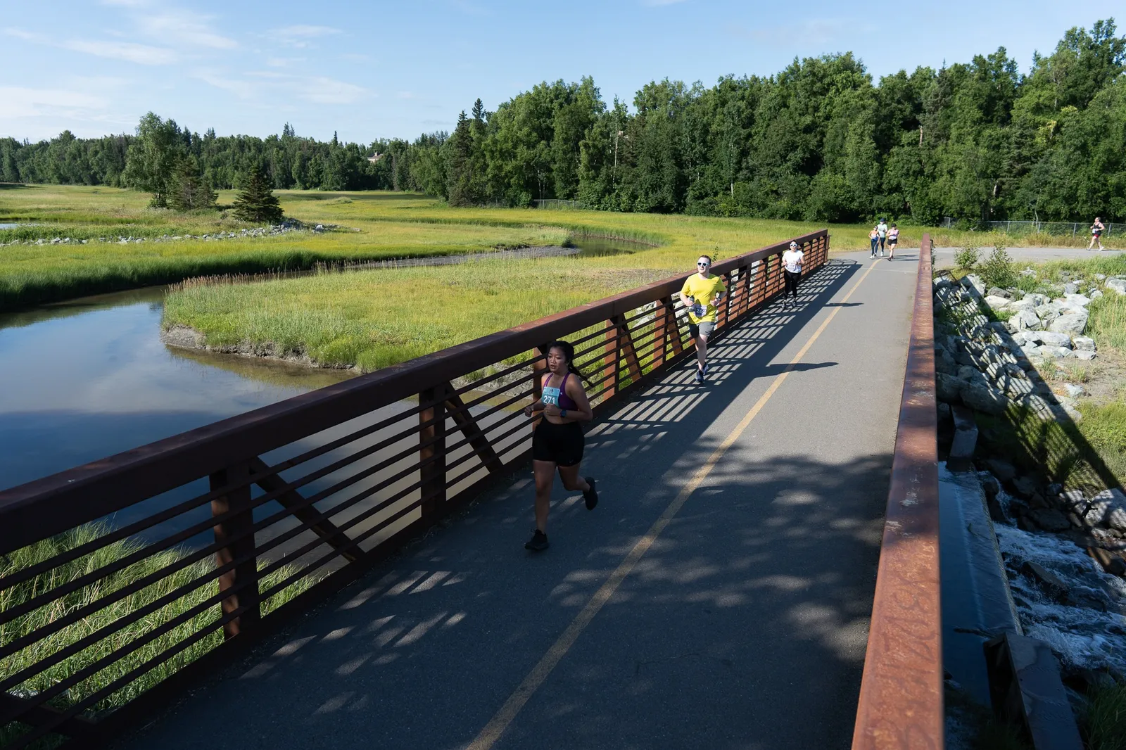 Runners on a bridge with a scenic natural landscape in the background.