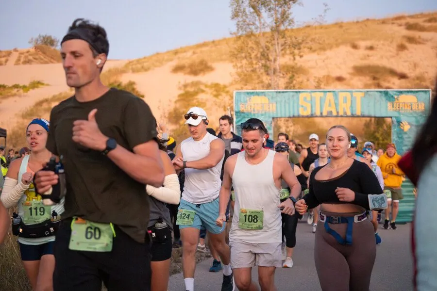 Runners starting a race under a 'START' banner, with sand dunes in the background.