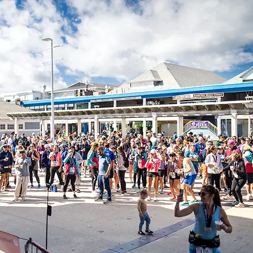 A large crowd of runners gathered outdoors, with some people in the foreground and a building in the background.