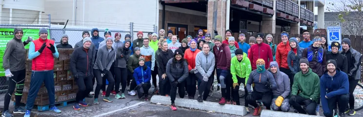 A large group of runners posing for a photo outdoors, dressed in winter running gear.