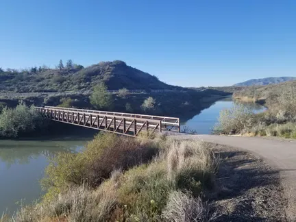 A scenic view of a bridge crossing a calm body of water, with rolling hills in the background under a clear blue sky.