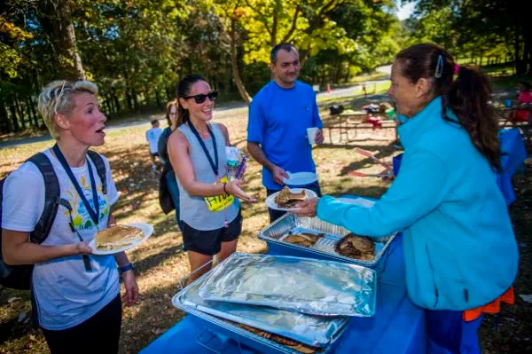 Runners receiving food at a post-race event, with one runner holding a plate of pancakes.