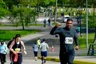 A runner in a dark long-sleeved shirt pumps his fist in the air as he runs uphill, with other runners behind him.