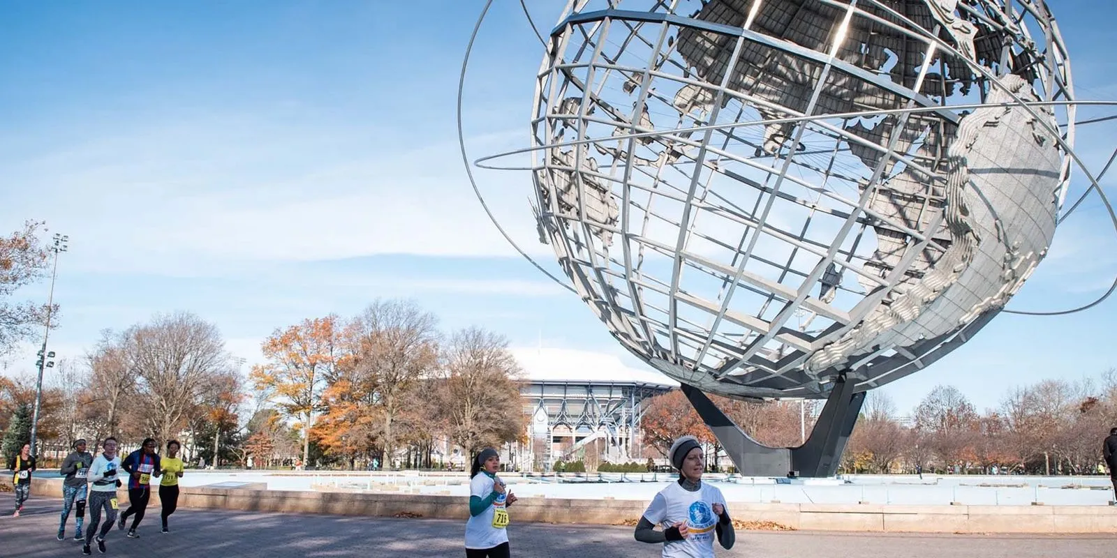Runners participating in a race with the Unisphere in Flushing Meadows Corona Park in the background.