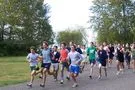 A group of runners, mostly young men, race down a tree-lined path.