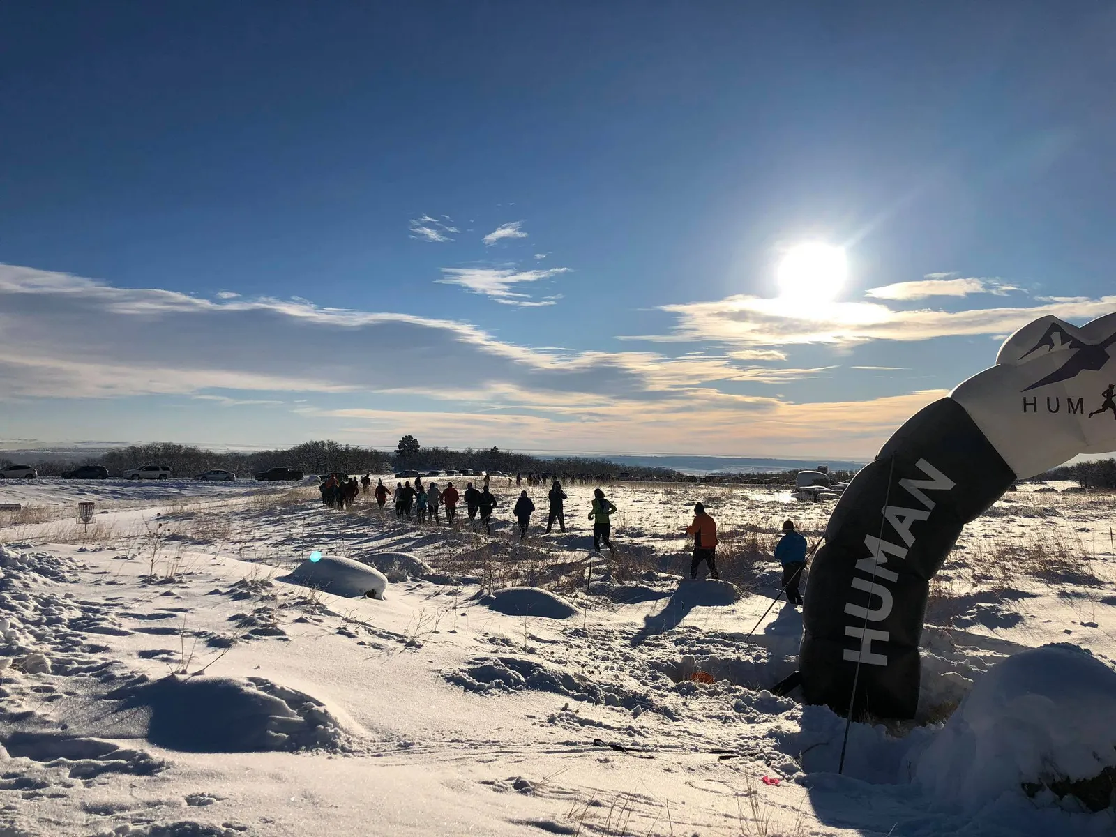 Runners crossing an inflatable archway on a snowy trail, with a bright sun in the sky.