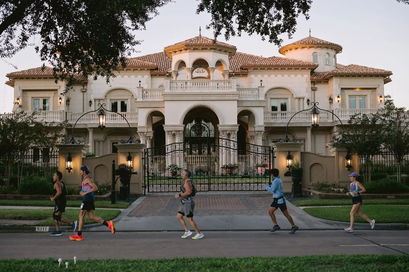 Runners on a road in front of a large, ornate mansion.