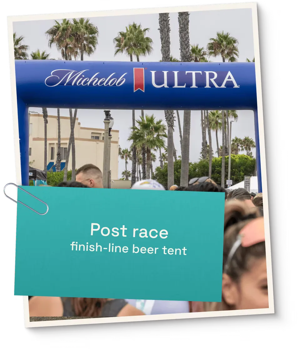 A crowd of people gathered under a Michelob Ultra archway, with a teal sign overlay that reads 'Post race finish-line beer tent'.