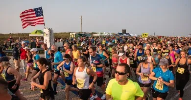 A large group of runners at the starting line of a race, with an American flag flying overhead.