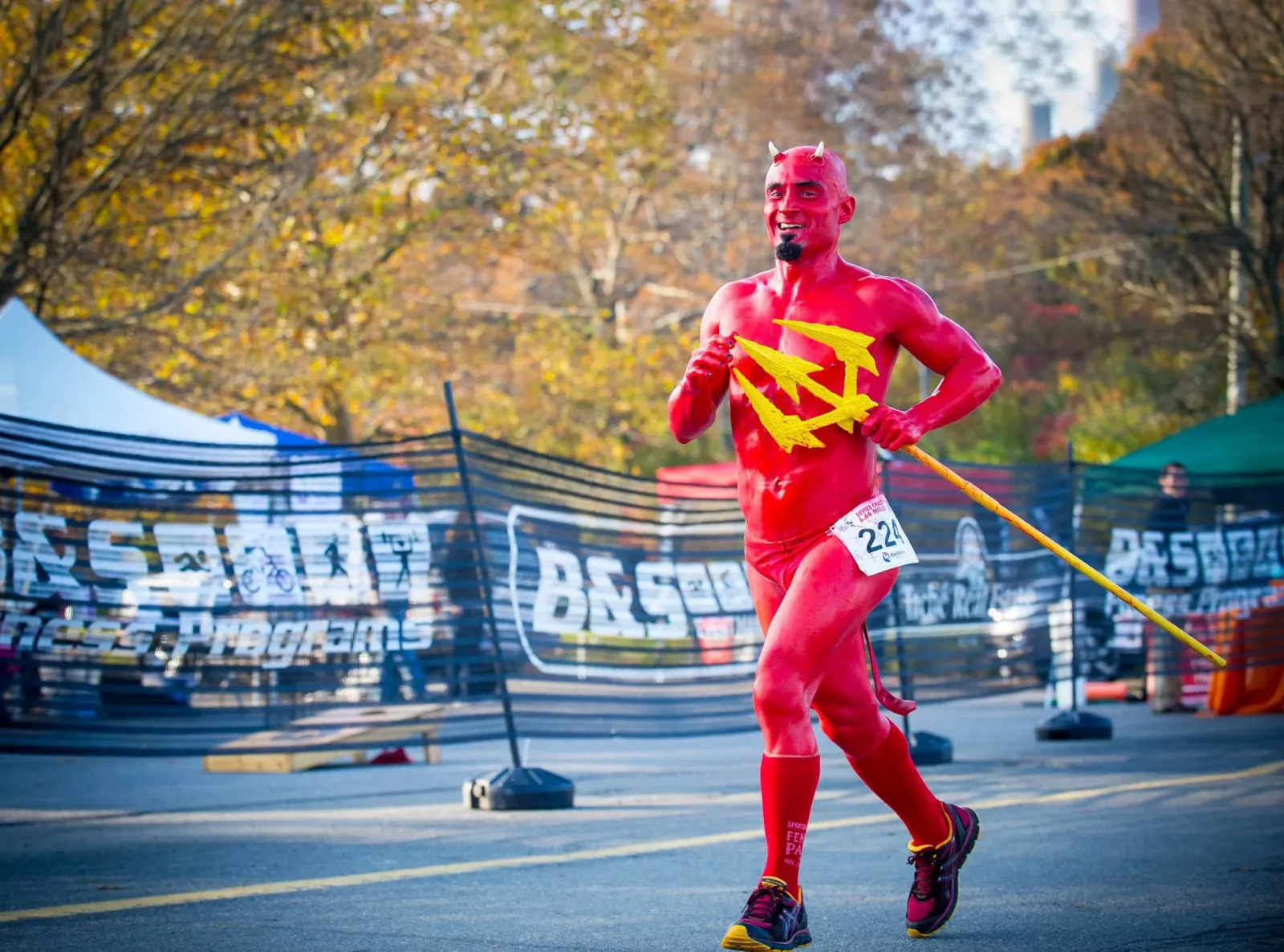 A runner dressed as a devil with red body paint and horns runs with a trident during the Tache Realty Wicked Half Marathon.