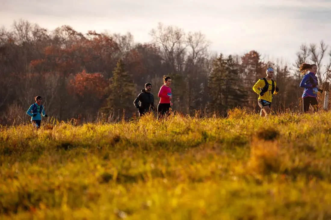 Runners on a grassy trail with trees in the background during a race.