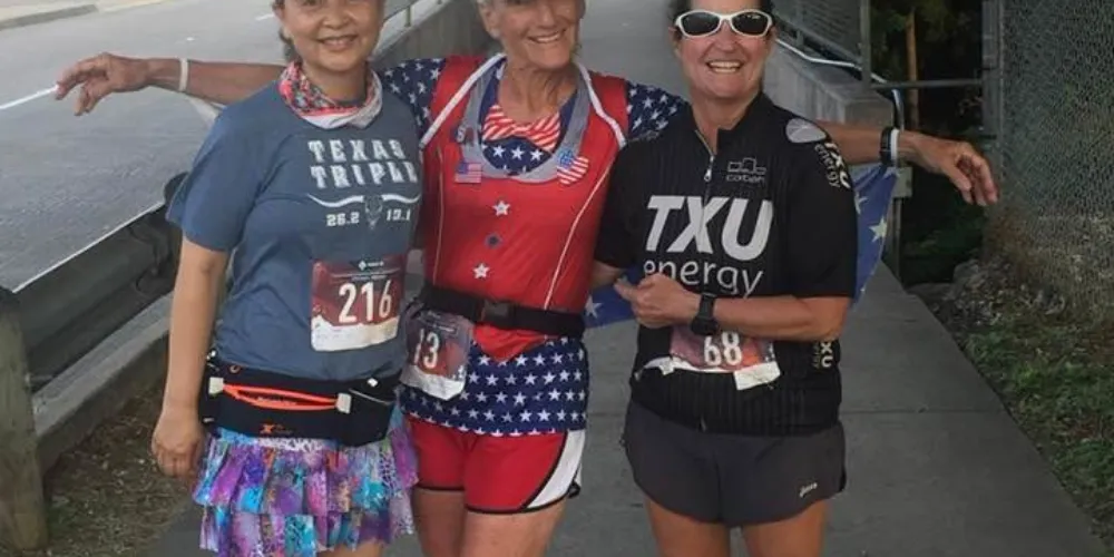 Three smiling runners pose for a photo after a race, two wearing patriotic-themed running gear.