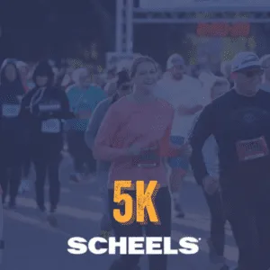 Runners at the start line of a 5K race, with a woman in a pink shirt smiling at the camera.