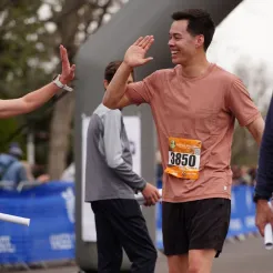 A male runner gives a high-five to another runner near the start line, both smiling.