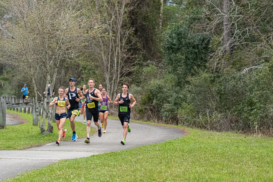 Runners on a paved path surrounded by trees and grass.