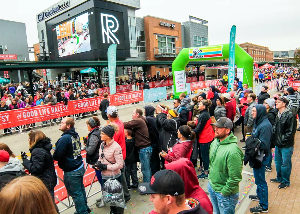 A large crowd of spectators and runners gathered at the start line of the Good Life Halfsy race, with an inflatable arch in the background.