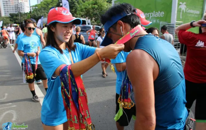 A race volunteer places a medal around the neck of a runner at the finish line.