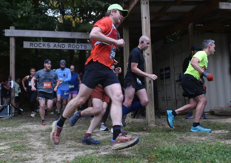 Runners starting a trail race under a wooden archway that says 'Rocks and Roots'.