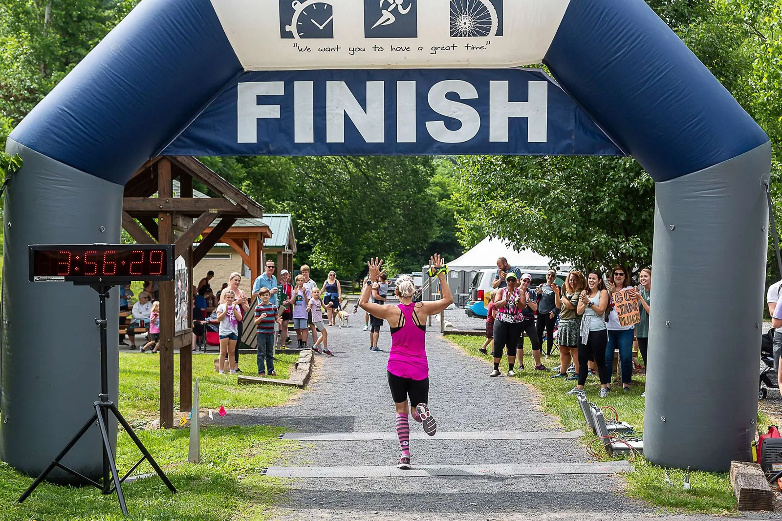 A runner crosses the finish line with arms raised in celebration, cheered on by a crowd under an inflatable arch.