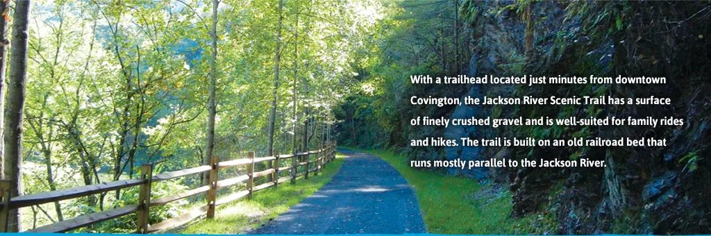 A scenic view of the Jackson River Scenic Trail, a paved path lined with trees and a wooden fence, with text describing the trail.