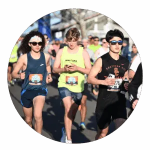 Three young men running in a race, with other runners in the background.