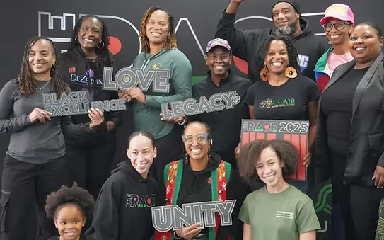 A diverse group of people smiling and holding signs that say 'BLACK EXCELLENCE', 'LOVE', 'LEGACY', and 'UNITY'.