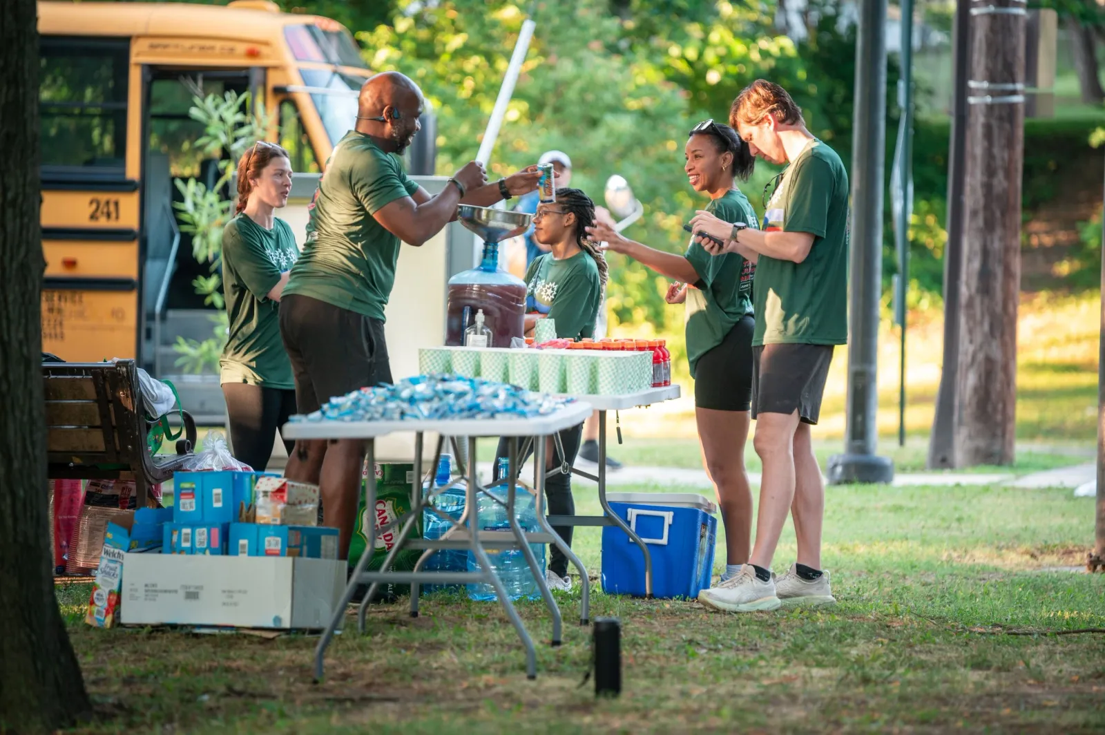 Volunteers in green t-shirts setting up a water station with a yellow school bus in the background.