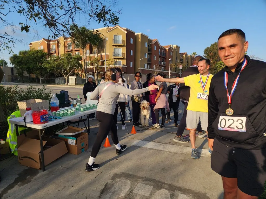 Runners and volunteers interacting at a race aid station, with some runners wearing medals.