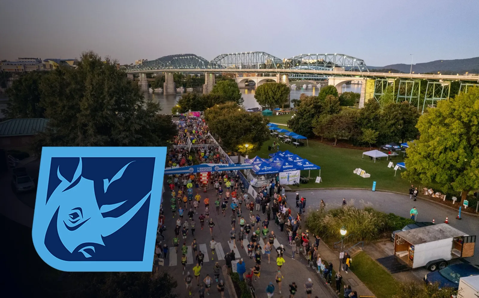 A large group of runners crossing a start/finish line with bridges and a river in the background.