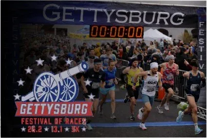 Runners starting a race at the Gettysburg Festival of Races, with a large crowd and a digital clock showing 00:00:00.