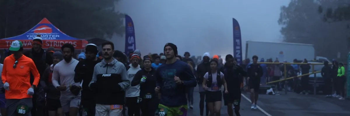 Runners gathered at the start line of the Tidewater Striders Dismal Swamp 50k, Half Marathon, and 50k Relay race, with tents and banners in the background.