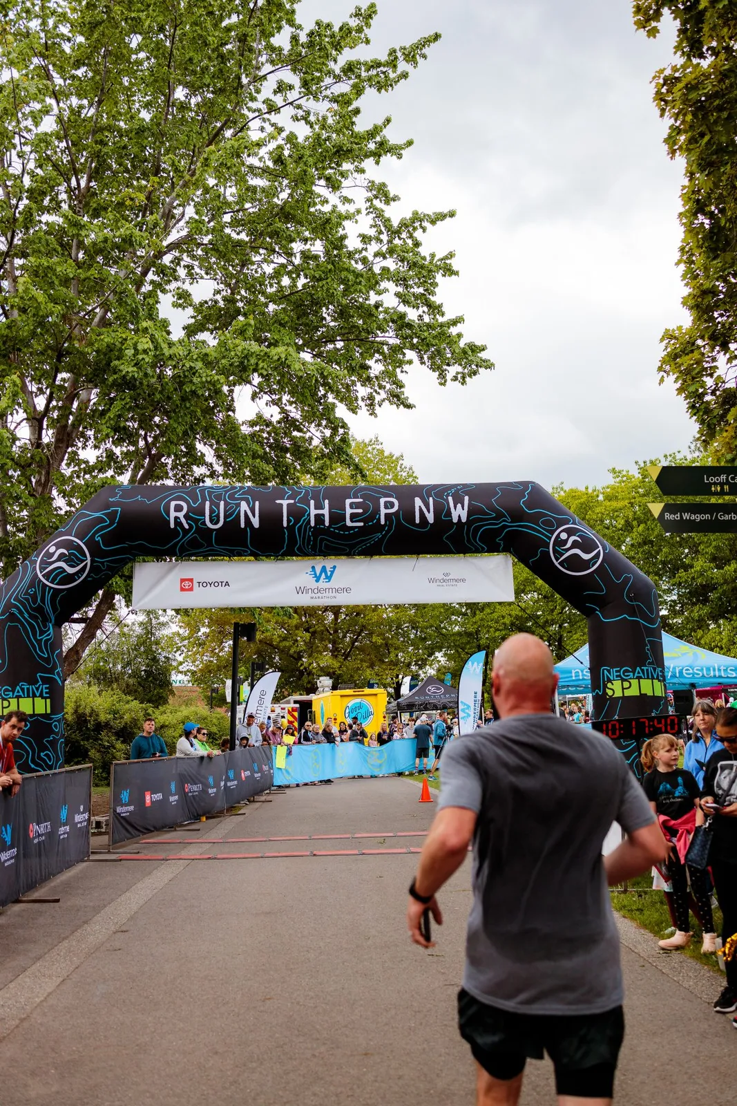 A runner approaches the finish line under a large inflatable archway with 'RUNTHEPNW' written on it. Spectators line the course in the background.