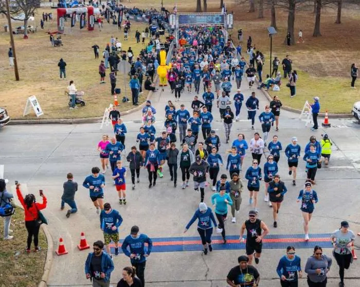 A large group of runners starting a race, with many participants in blue shirts visible, heading towards the camera.
