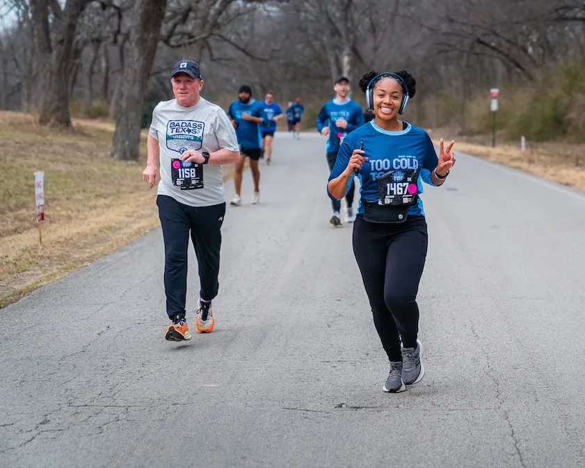 Two runners smiling and running on a paved road during the Too Cold to Hold 5k/10k/Half Marathon.