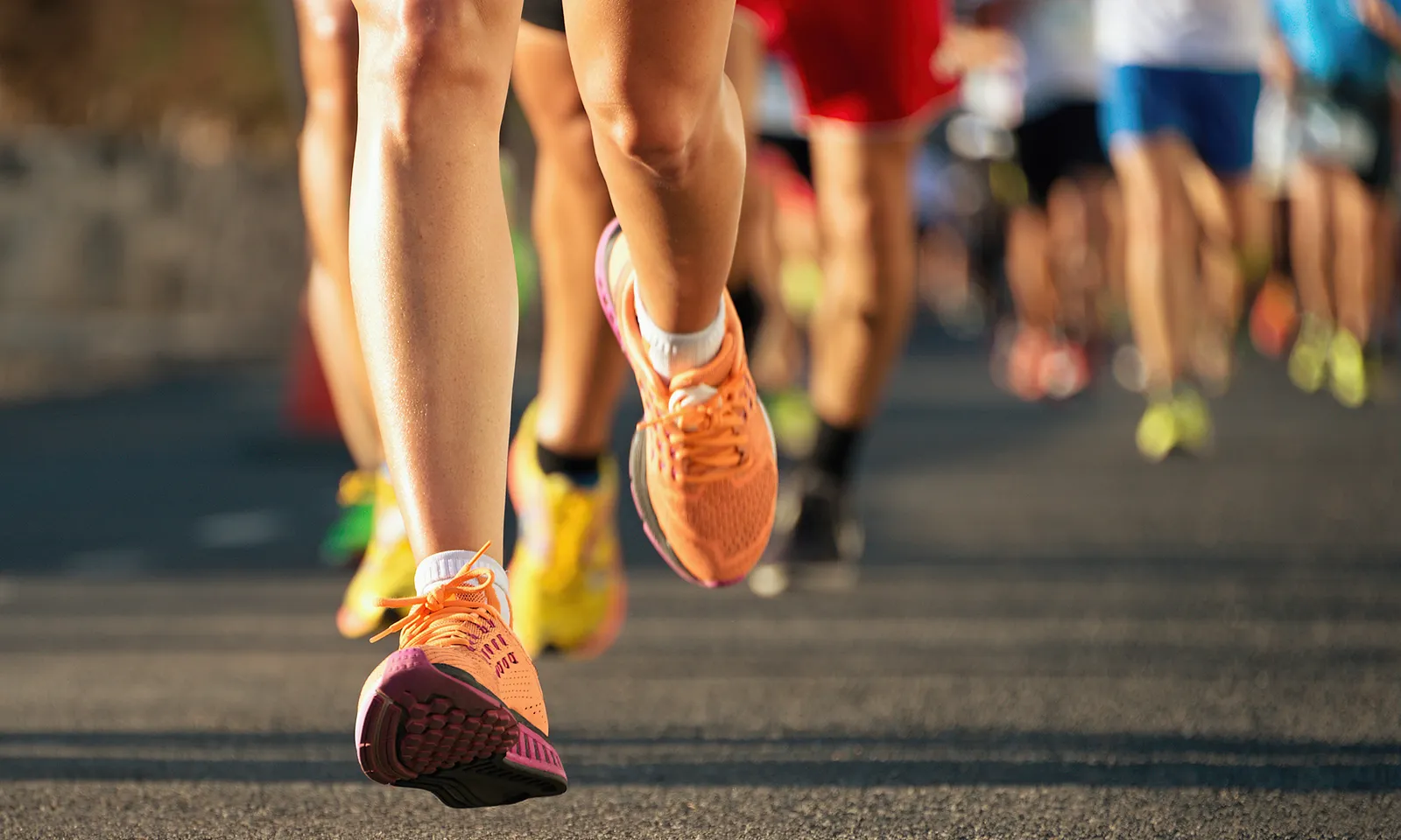 Close-up of runners' legs and orange shoes on a road during a race.