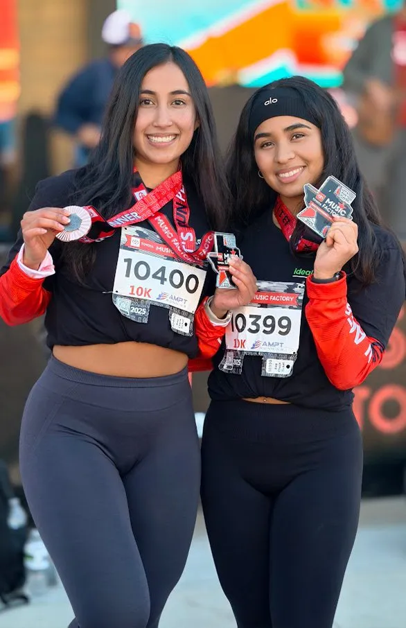 Two smiling women wearing race medals and bibs, celebrating after a run.