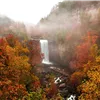Waterfall surrounded by colorful autumn trees with mist in the background.