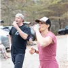 Two runners wearing hats and drinking from cups, with trees and cars in the background.