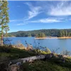 Scenic view of a lake surrounded by forested hills under a blue sky with wispy clouds.