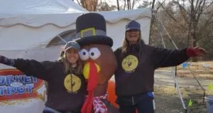 Two smiling people pose with a turkey mascot at the Turkey Trot race.