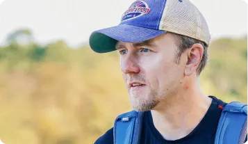 A male runner wearing a blue and tan baseball cap and a black t-shirt, looking off to the side with a focused expression.