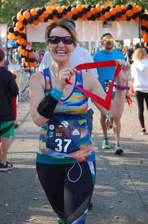 A smiling female runner holds up her medal after crossing the finish line at the Upper Cumberland Haunted Half Marathon.